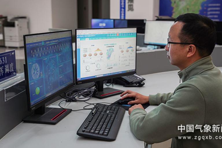 A person in an office analyzes data on two computer monitors displaying graphs and charts.