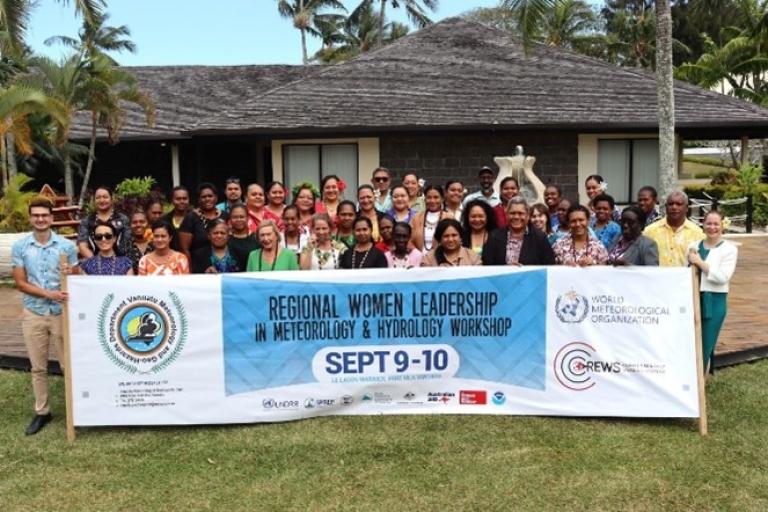 Group photo of attendees at the Regional Women Leadership in Meteorology & Hydrology Workshop, holding a banner with event details and logos, set outdoors with greenery and a building in the background.