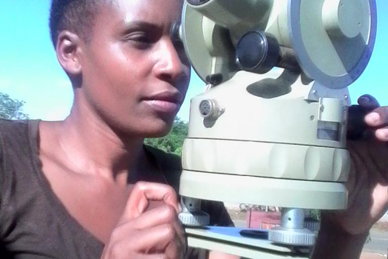 A person using a theodolite outdoors under a clear blue sky.