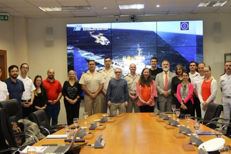 Group of people posing in a conference room with a large screen displaying a ship at sea in the background.