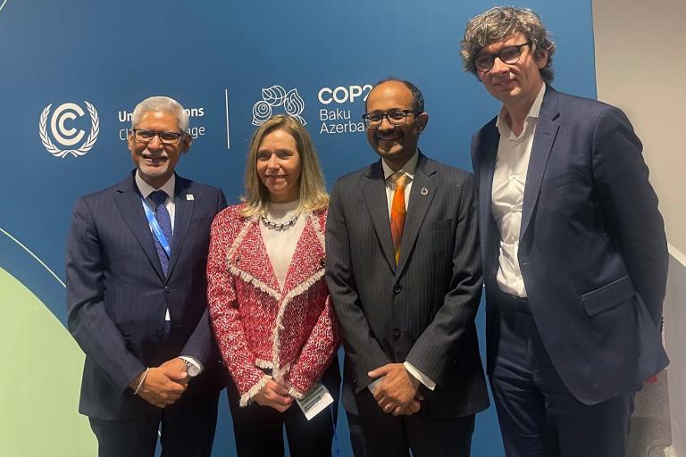Four people in business attire stand in front of a COP28 banner with the UN logo.