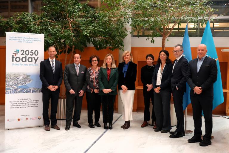 A group of people in business attire stand indoors next to banners and flags, posing for a photo.