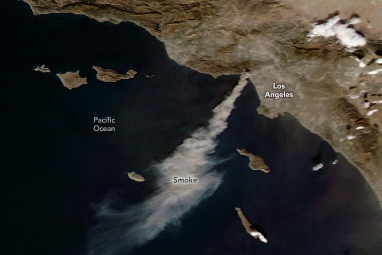Satellite image showing smoke from wildfires near Los Angeles drifting over the Pacific Ocean. Land features and labels for Los Angeles and Pacific Ocean are visible.