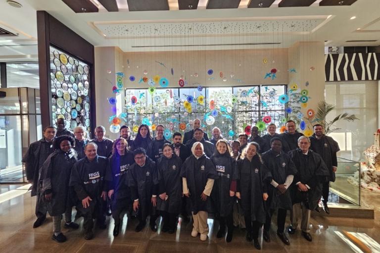 A group of people wearing matching dark outfits pose together indoors in front of a colorful wall display featuring circular designs.