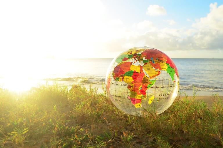An inflatable globe sits on grass near a beach, with the ocean and sky in the background.