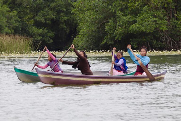 People paddling two canoes on a calm lake surrounded by lush greenery.