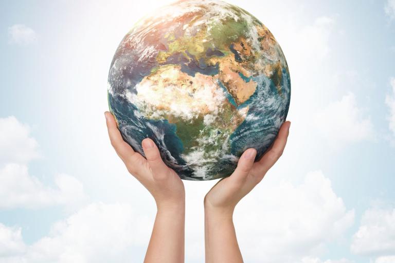 Hands holding up a globe against a cloudy sky background.