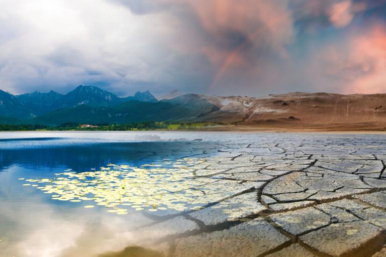 A split landscape shows a serene lake with mountains on the left and cracked, dry earth under a red sky on the right, illustrating a contrast between lush and arid environments.
