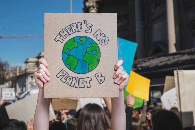 A person holds a sign with a drawing of Earth and the words “There’s No Planet B” at a public protest or demonstration.