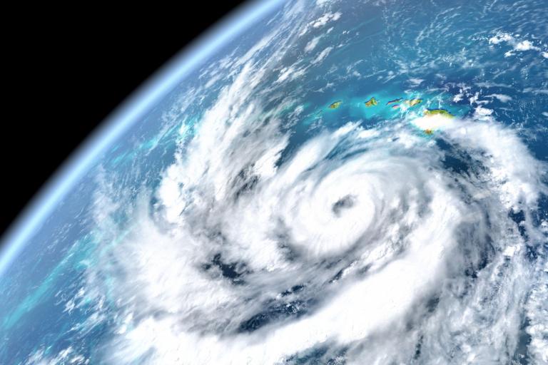 Satellite view of a swirling hurricane over the ocean with a visible coastline in the top right, showcasing the storm's spiral cloud formation.