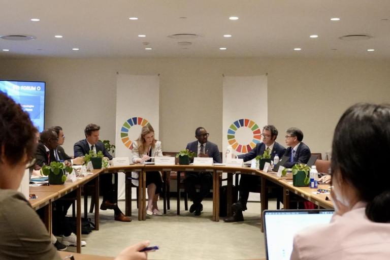 A group of diverse individuals in formal attire sit around a U-shaped table in a conference room.