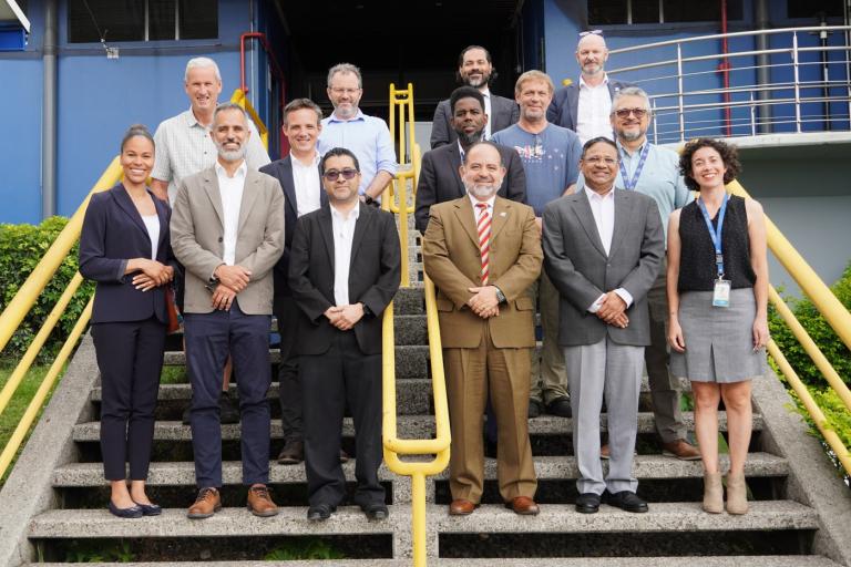 A group of fourteen people poses for a photo on outdoor stairs in front of a building, dressed in business and casual attire.