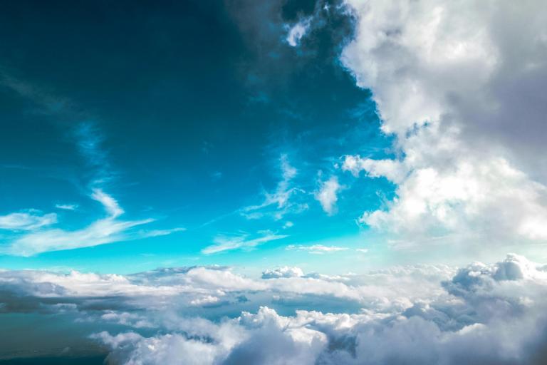 A view of the sky with white and grey clouds under a blue sky, seen from above or within the clouds.