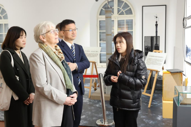 Four people stand together in a museum or gallery, listening to a guide explain framed photographs on the wall.