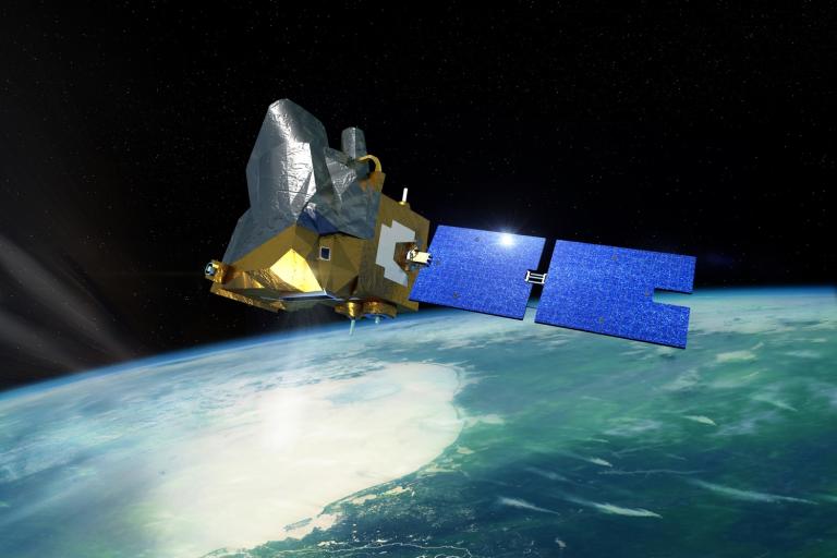 A satellite with blue solar panels orbits above Earth, with a view of clouds, land, and ocean below against the blackness of space.