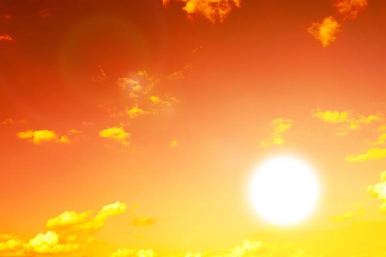 Bright sun in a clear orange sky with scattered yellow clouds, creating a warm and glowing atmosphere.