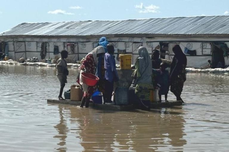 Families wade through floodwaters to access a water point