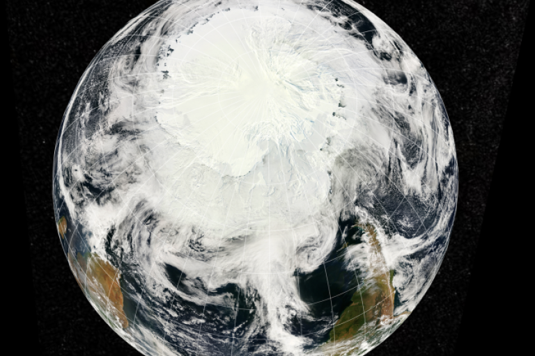 A satellite view of Earth focused on the South Pole, showing Antarctica covered in ice and clouds swirling over the Southern Hemisphere.