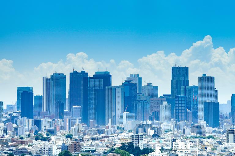 A city skyline with numerous modern skyscrapers and high-rise buildings under a blue sky with some clouds.