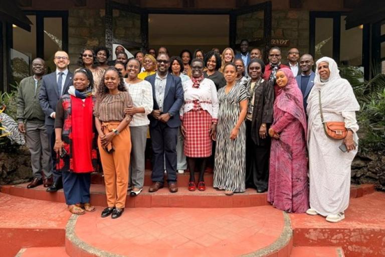 A large, diverse group of people stands together on red steps in front of a building, posing for a group photo.