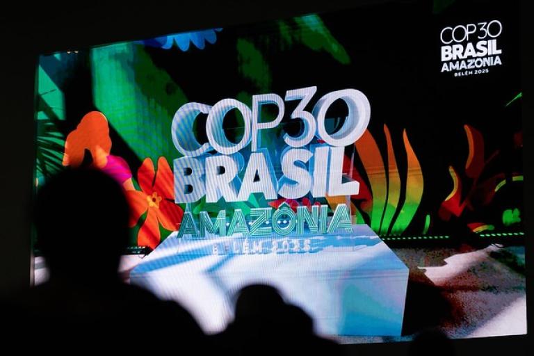 A large screen displays the COP30 Brasil Amazonia Belém 2025 logo with colorful foliage and silhouettes of people in the foreground.