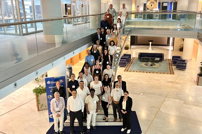 A group of people pose for a photo on a staircase and the marble floor of a spacious, modern lobby with seating and decorative elements.