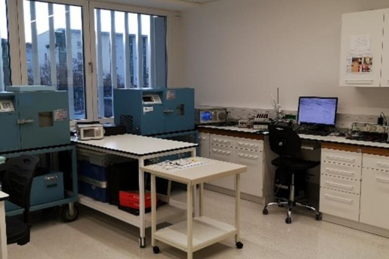 Laboratory room with blue scientific equipment, workstations, computers, white cabinets, and large windows letting in natural light.