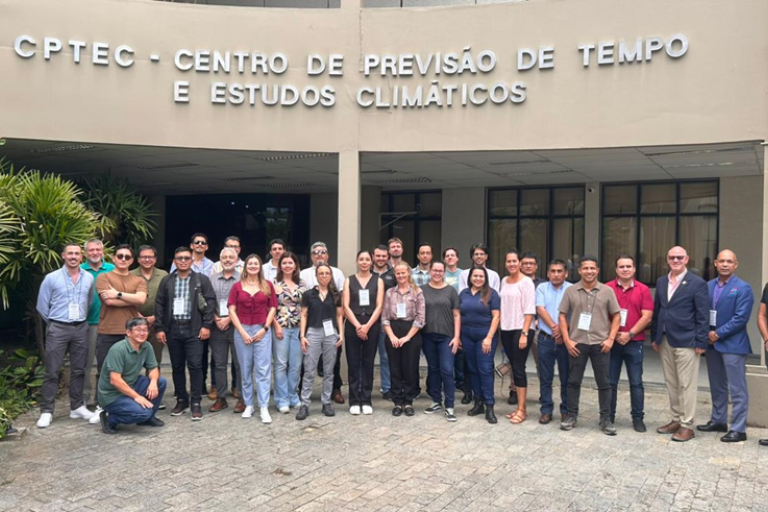 A group of people poses for a photo in front of the CPTEC - Centro de Previsão de Tempo e Estudos Climáticos building.