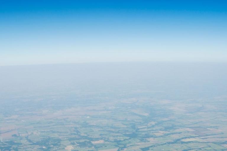 Aerial view of farmland with a clear blue sky above and a hazy horizon in the distance.