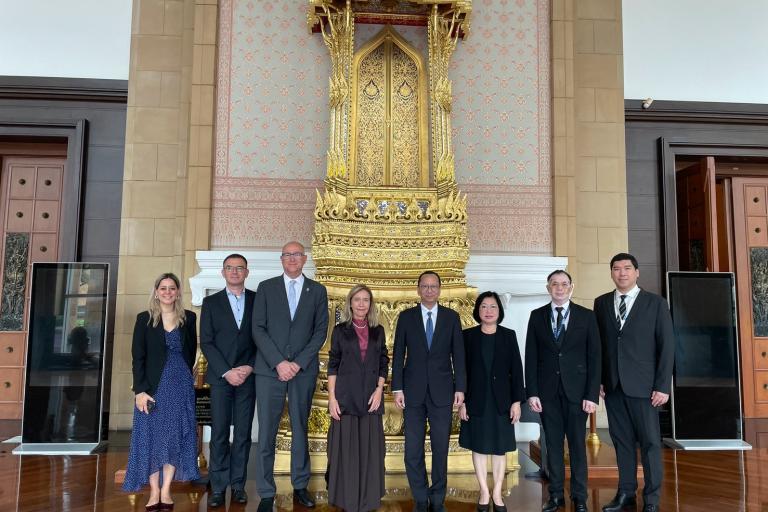 Eight people in formal business attire pose in a line in front of an ornate, gold-leafed ceremonial throne.