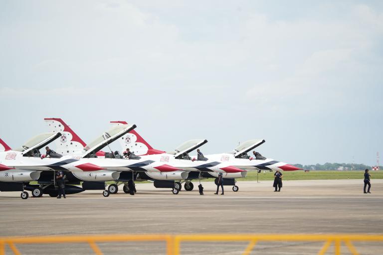 Four F-16 Fighting Falcon aircraft from the USAF Thunderbirds parked on a flight line with crew members standing nearby.