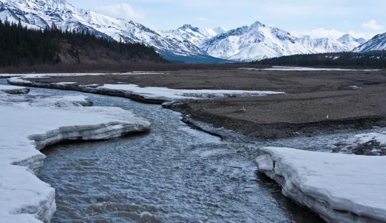 A river in the snow with mountains in the background.