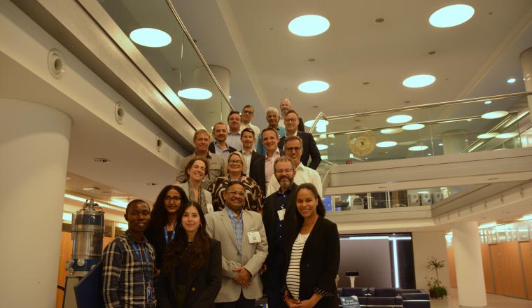 Group of diverse people smiling for a photo in a modern lobby with circular overhead lighting.