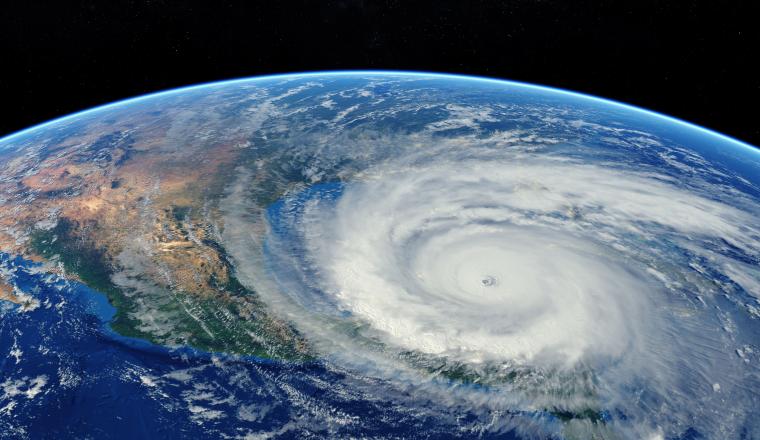 Satellite view of a large, swirling hurricane over the ocean near a continent, with a clear eye at the center and surrounding cloud bands.