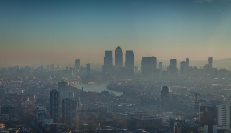 A hazy cityscape with modern high-rise buildings and a river running through the urban area under a blue sky.