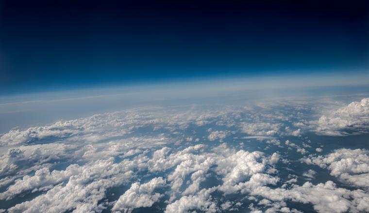 View of white clouds covering the Earth's surface with a gradient blue sky above, taken from a high altitude, possibly from an airplane or stratospheric balloon.