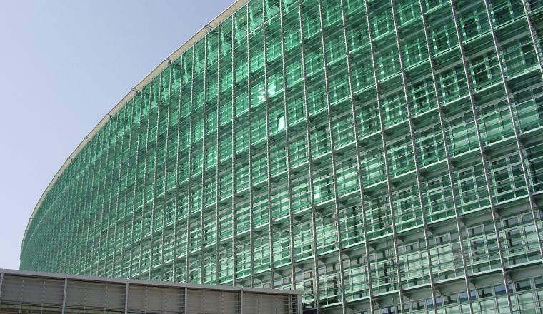A tall, modern glass building with a curved facade and grid-like window patterns, shown against a clear blue sky.