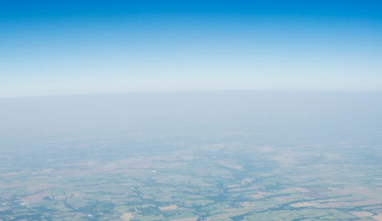 Aerial view of farmland with a clear blue sky above and a hazy horizon in the distance.