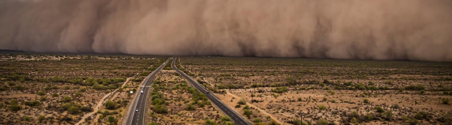 A massive dust storm approaching a highway running through a desert landscape.