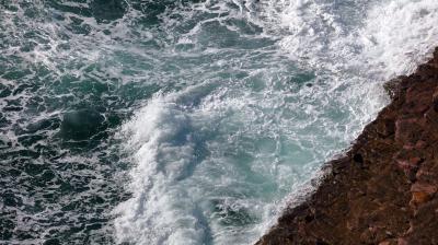 An aerial view of a wave crashing over a cliff.