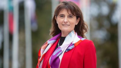 A woman in a red jacket standing in front of flags.