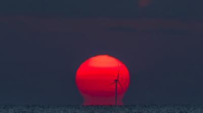 A red sunset with a wind turbine in the background.
