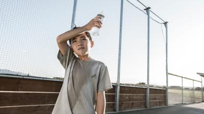A boy drinking water from a bottle on a baseball field.