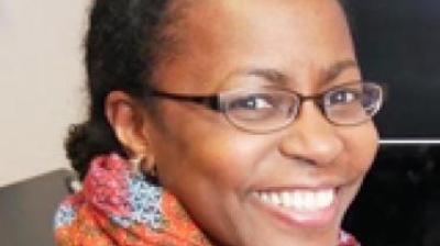 A woman wearing glasses and a scarf smiles in front of a computer.