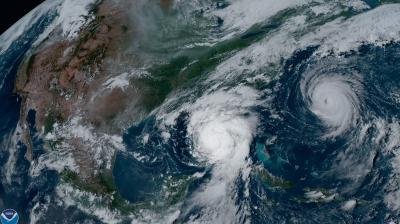 Satellite image showing two hurricanes over the Atlantic Ocean and the Gulf of Mexico, with visible cloud formations and weather patterns over the eastern United States and the Caribbean.