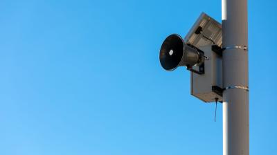 A loudspeaker attached to a pole is set against a clear blue sky.