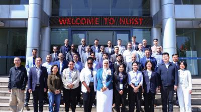 A group of people stands in front of a building with a sign that reads "Welcome to NUIST." They are posing for a group photo on steps outside the entrance.