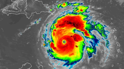 Satellite image of a large, well-defined hurricane with a visible eye, near the Caribbean islands, displaying intense colors indicating varying levels of precipitation and storm intensity.
