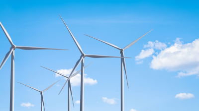 A row of wind turbines against a clear blue sky with scattered clouds.