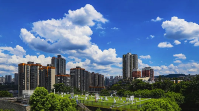 Urban skyline with tall residential buildings, green spaces, and a cemetery in the foreground under a partly cloudy sky.